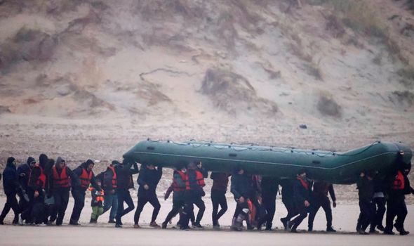La police française se tient à proximité d'un groupe de plus de 40 migrants qui courent avec un canot pneumatique.