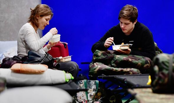  Une femme et un jeune homme qui ont fui l'Ukraine sont assis sur des lits de camp et mangent dans un gymnase d'école transformé en abri d'urgence.