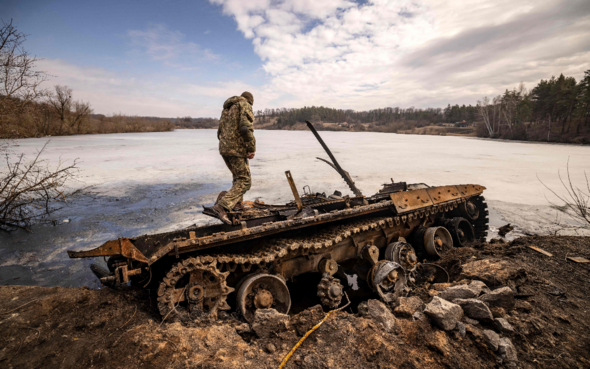 Un soldat ukrainien se tient à côté d'un char russe détruit.