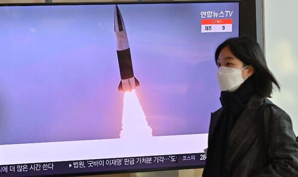 Une femme passe devant un écran de télévision montrant une émission de nouvelles avec des images d'archives d'un test de missile nord-coréen
