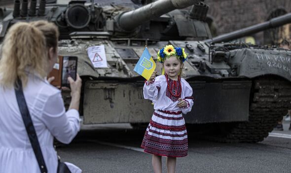 Petite fille avec une couronne de fleurs se faisant prendre en photo près d'un char d'assaut.