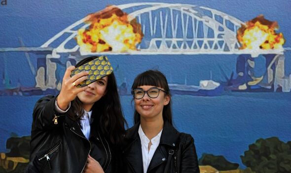 Des personnes prennent des photos sur fond de timbres, représentant le pont de Crimée en flammes.