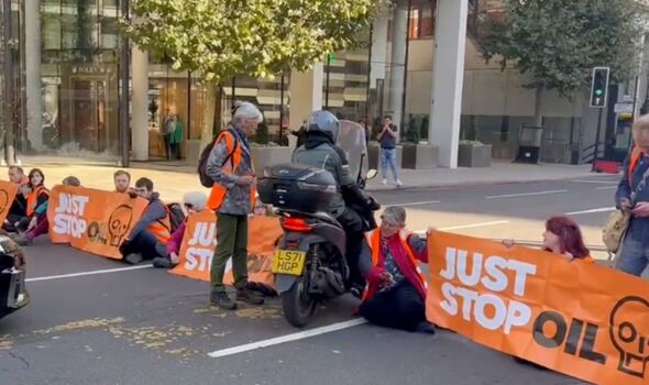 Des militants portant des gilets orange haute visibilité se sont assis sur la route en tenant des bannières 