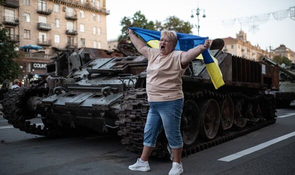 Une femme tenant un drapeau ukrainien à côté d'un char d'assaut.