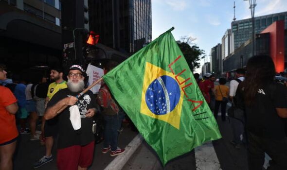 Homme tenant un drapeau brésilien sur lequel est écrit Lula