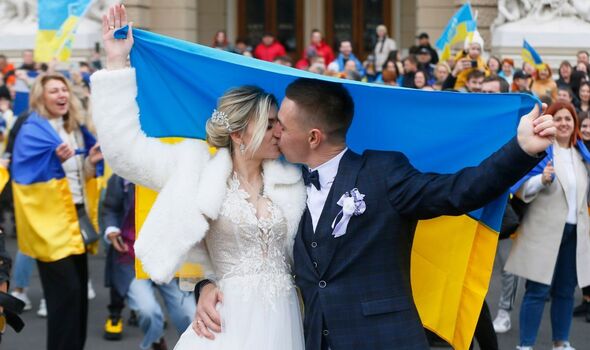 Photo d'un couple heureux le jour de leur mariage, s'embrassant avec un drapeau ukrainien. 