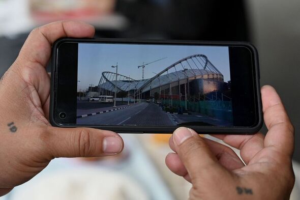 Un homme tient un téléphone avec une photo du stade de la Coupe du Monde dans ses mains.