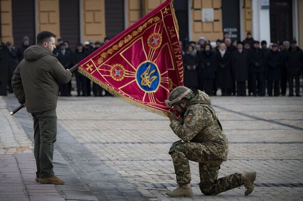 Un soldat ukrainien embrasse un drapeau tenu par Zelensky lors de l'anniversaire 
