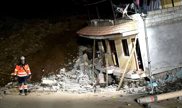 Un secouriste marche à côté d'une maison effondrée tout en cherchant dans la nuit 