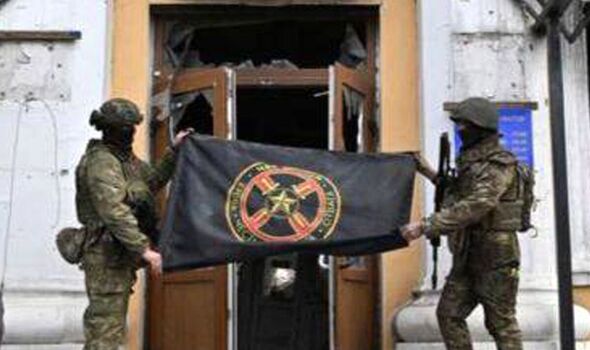 Des mercenaires brandissent un drapeau du groupe Wagner devant le bâtiment administratif de Bakhmut cette semaine 