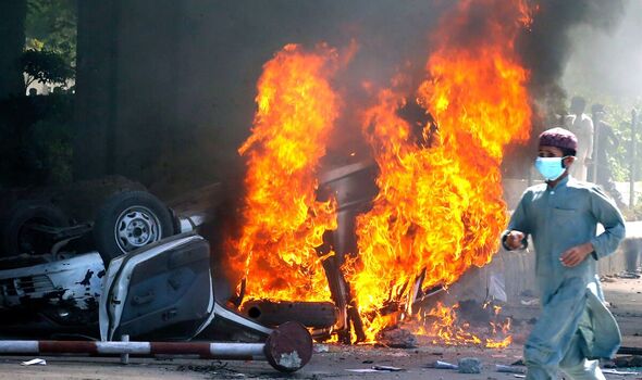 Un homme passe devant une voiture en feu incendiée par des partisans en colère de Khan à Peshawar